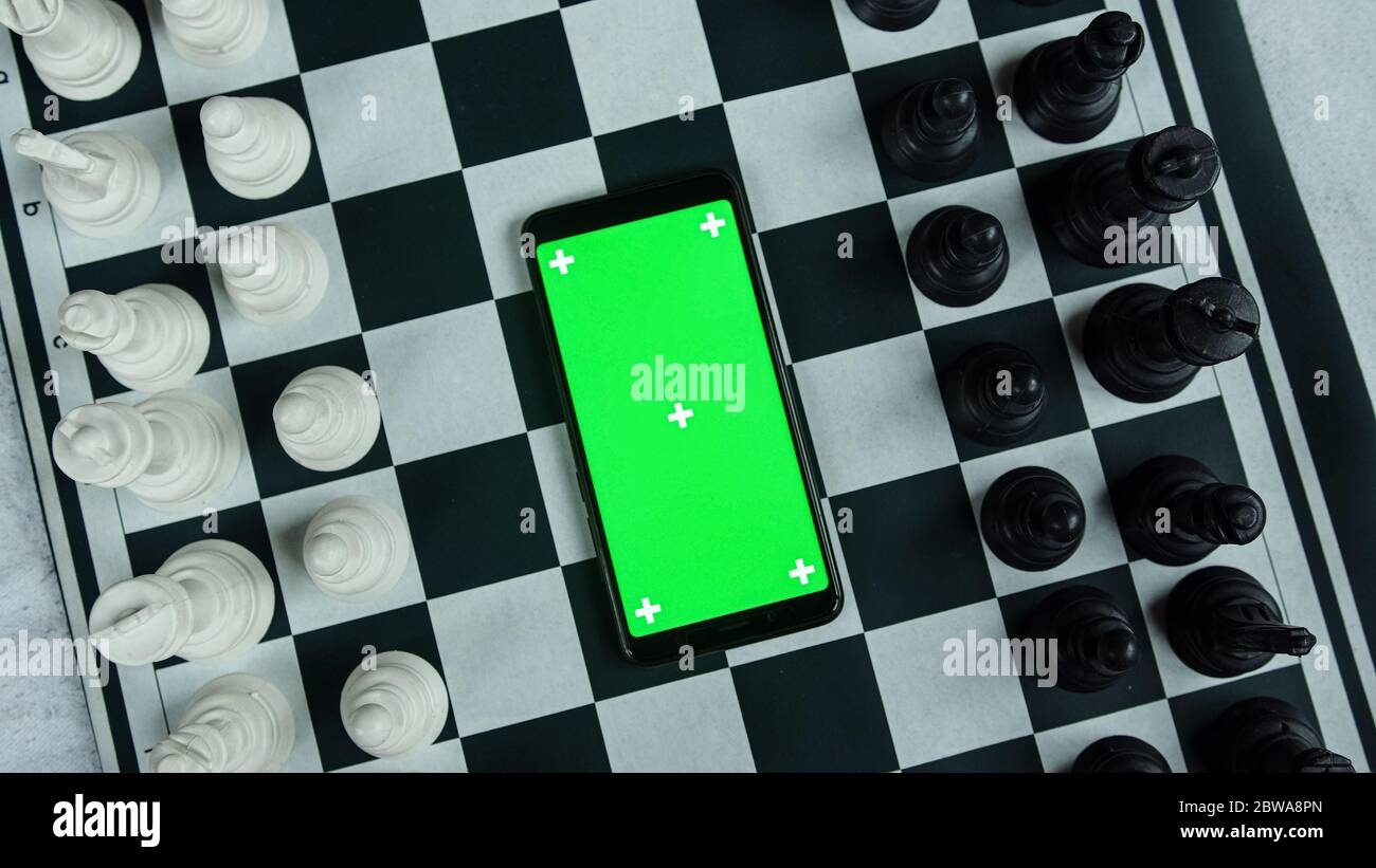Black and white chess pieces and a smart green screen phone in the middle. Chess application concept Stock Photo