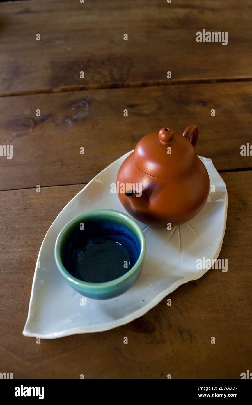 Chinese red clay pot and small cup on handmade ceramic leave shaped plate on wooden table Stock Photo