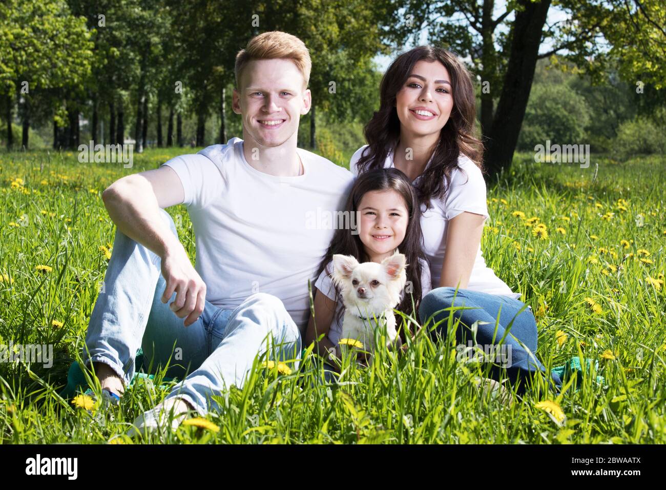 Happy smiling family of parents and daughter with pet dog in summer park Stock Photo