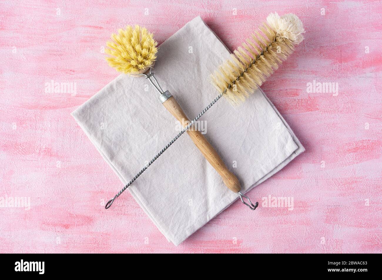 Bottle and dish brush on gray cloth isolated on pink background. Zero waste and natural ingredients home cleaning concept. Top view, layout. Stock Photo