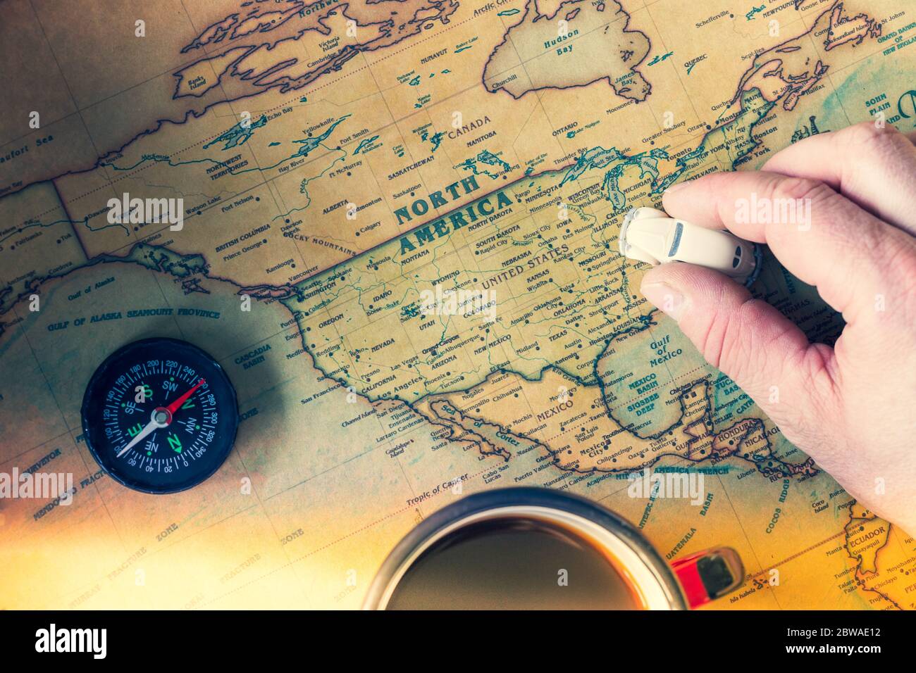 An old map of America with compass, a cup of tea and toy car in hand. Concept of traveling around the country in an old school style Stock Photo