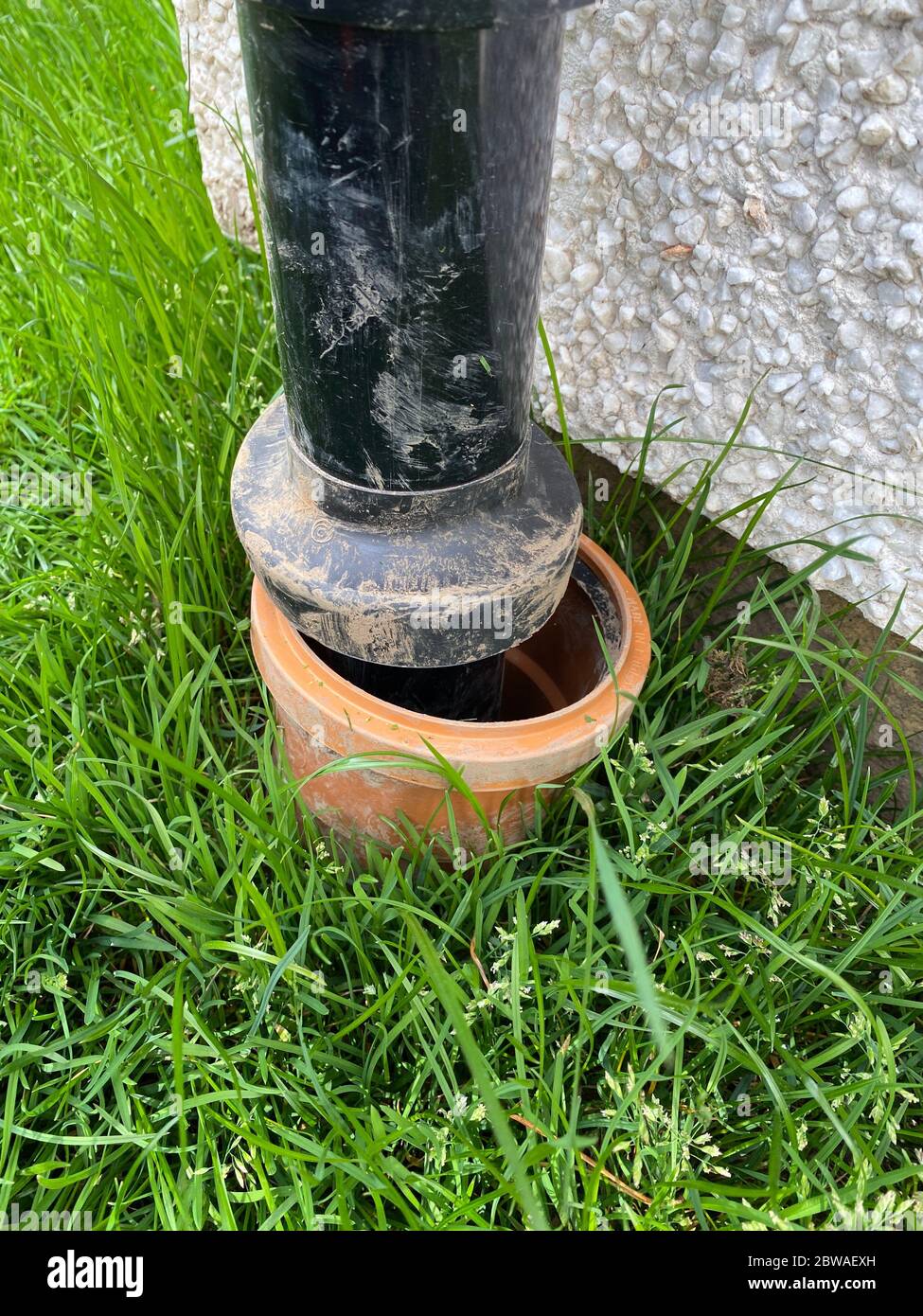 Rainwater drain downpipes black connection to underground drainage at house Stock Photo