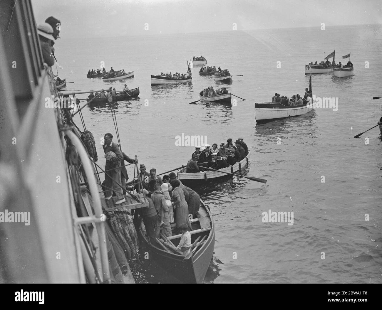 no further information available Row boats bring passengers to an ocean liner moored at sea. c.1920 Stock Photo