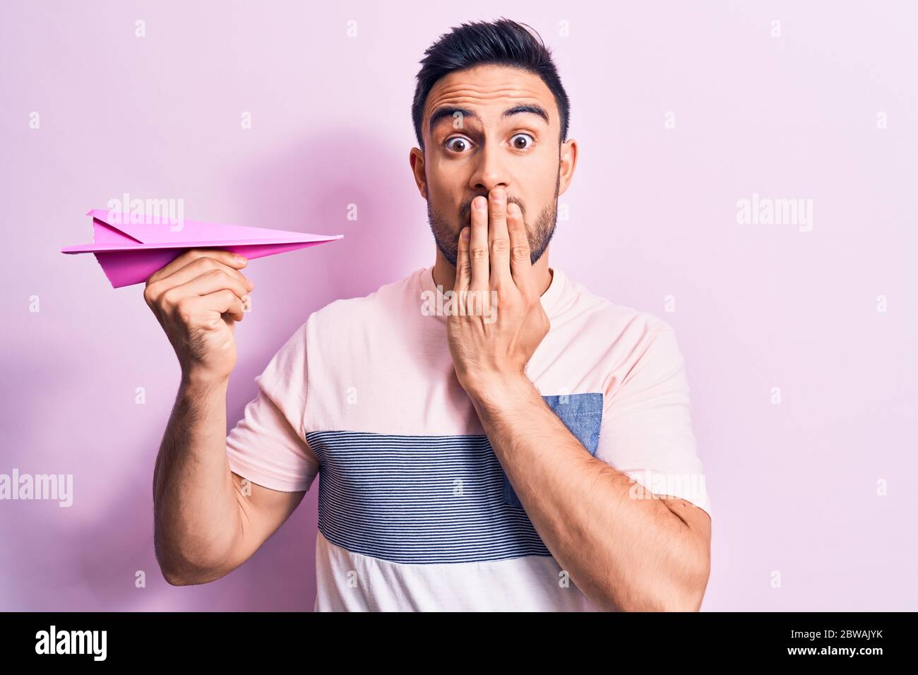 Afraid Paper Young handsome man with beard holding pink paper airplane over isolated ...