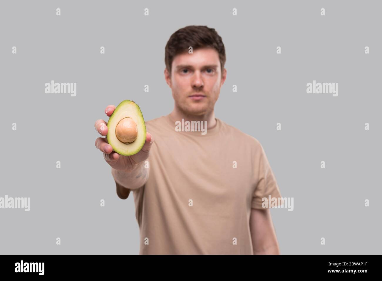 Man Showing Avocado Serious Face Isolated. Avocado Cut in Half. Healthy Food, No Avocado, Stop Avocado Concept Stock Photo