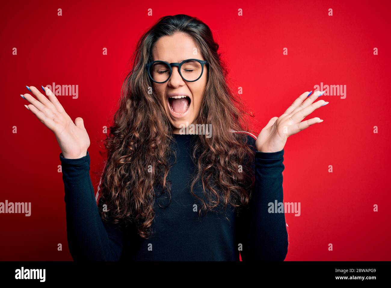 Young beautiful woman with curly hair wearing sweater and glasses over ...
