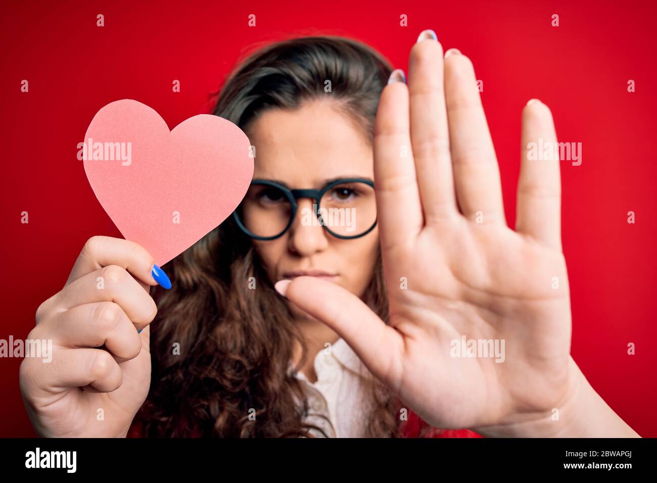 Young beautiful woman with curly hair holding paper heart over isolated ...