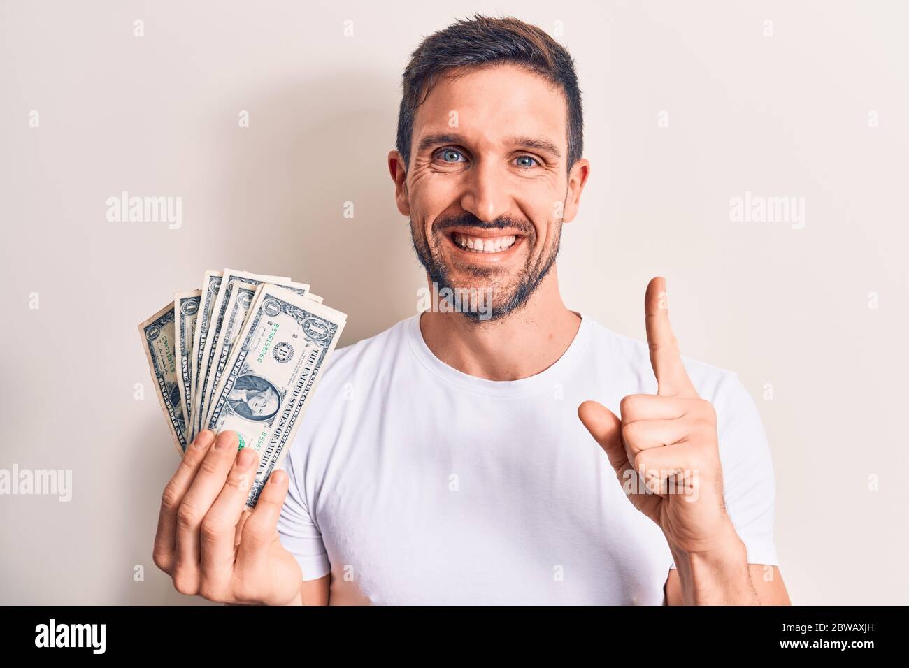 Young handsome man holding bunch of dollars banknotes over isolated ...