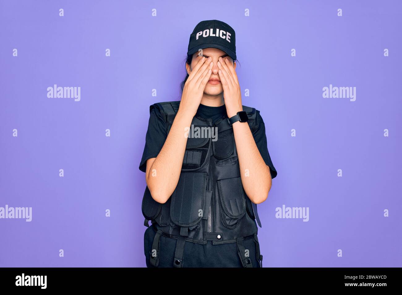 Young police woman wearing security bulletproof vest uniform over purple background rubbing eyes for fatigue and headache, sleepy and tired expression Stock Photo