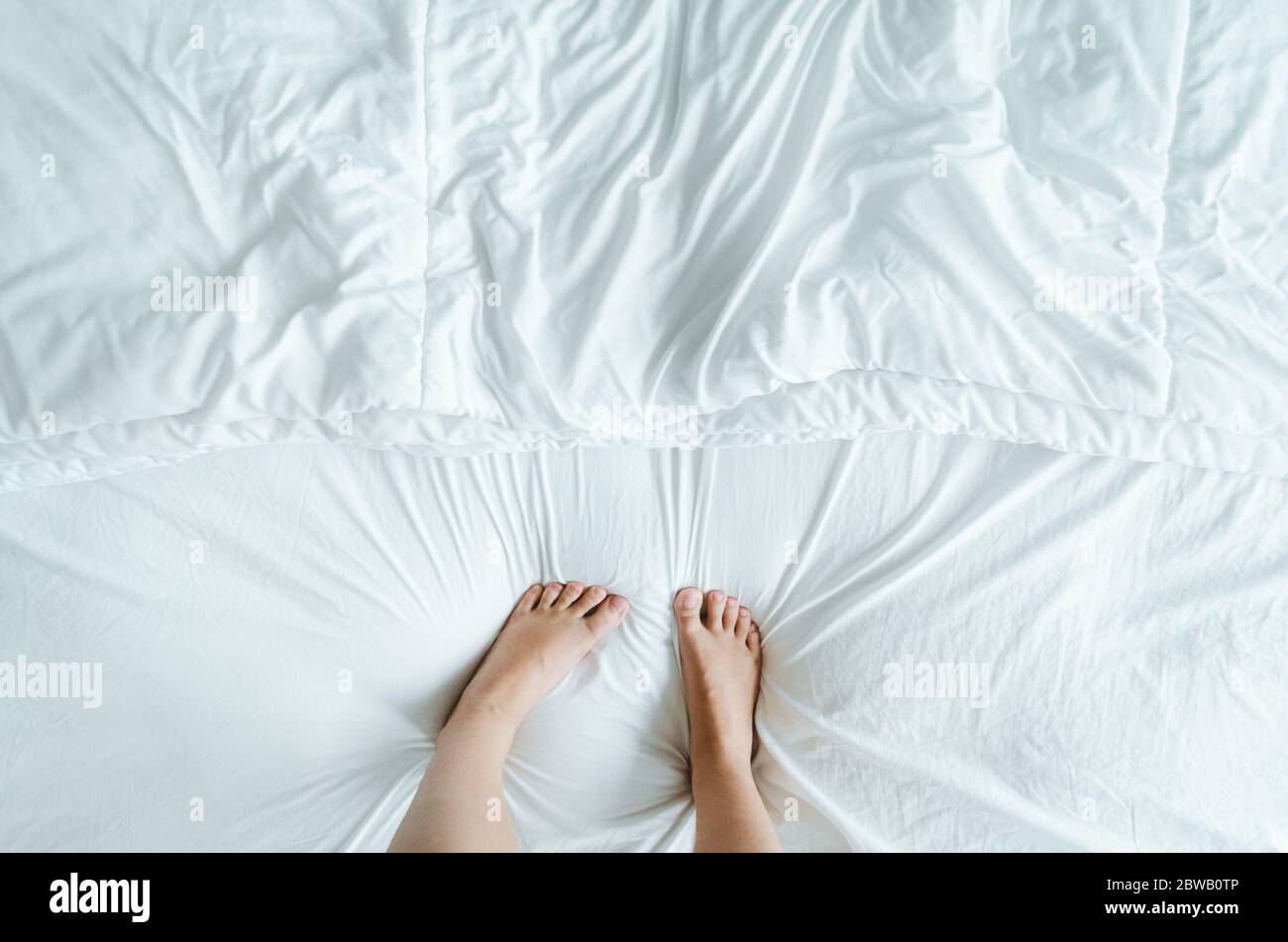 Feet and toes playfully stepping on the white wrinkly sheets of the bed