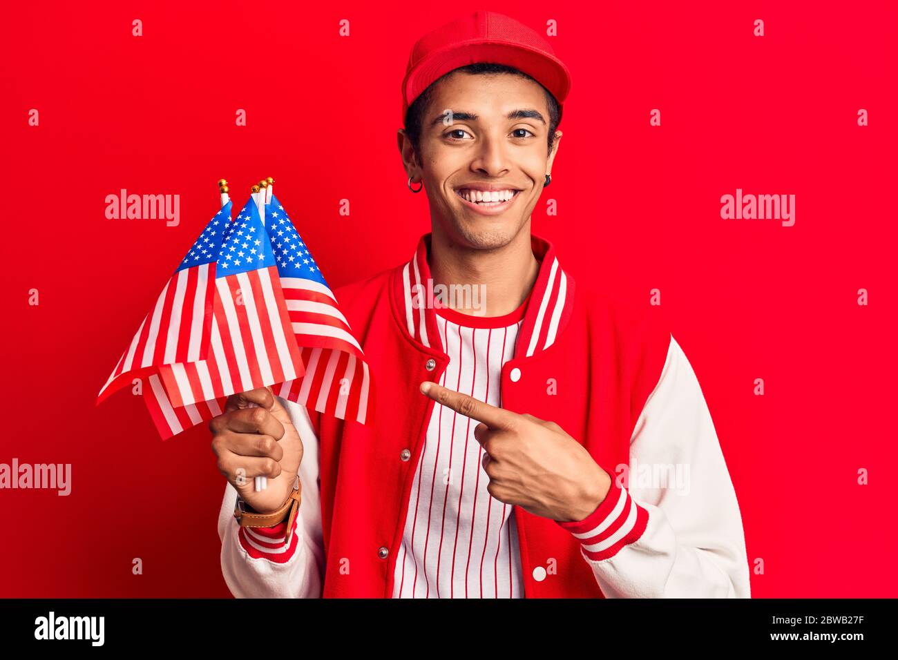 Young african amercian man wearing baseball uniform holding america flags smiling happy pointing with hand and finger Stock Photo