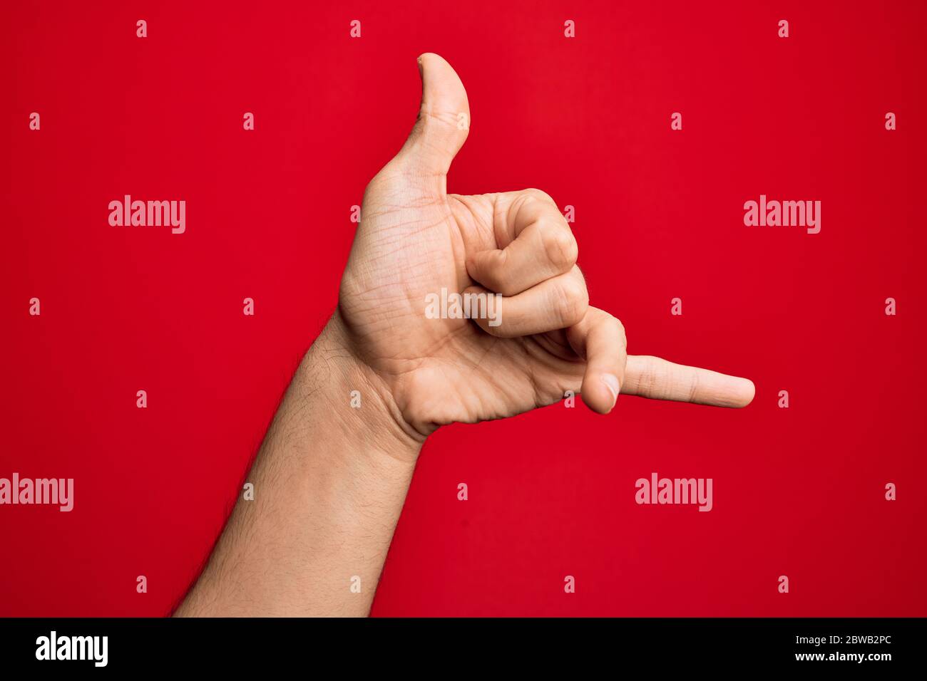 Hand of caucasian young man showing fingers over isolated red background gesturing Hawaiian shaka greeting gesture, telephone and communication symbol Stock Photo