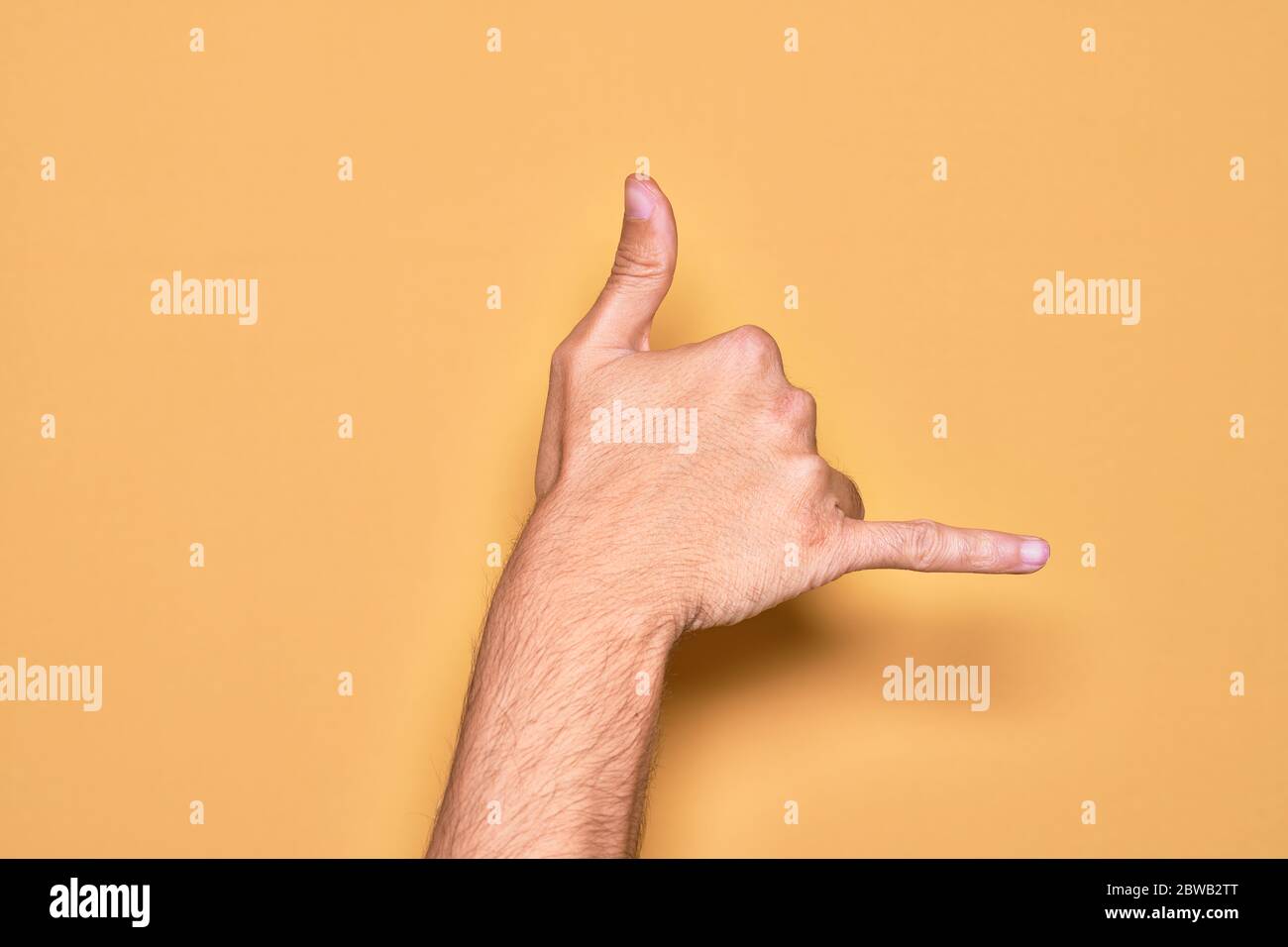 Hand of caucasian young man showing fingers over isolated yellow background gesturing Hawaiian shaka greeting gesture, telephone and communication sym Stock Photo