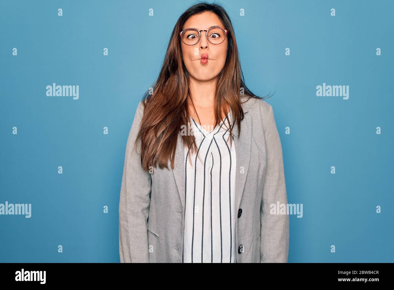Young hispanic business woman wearing glasses standing over blue ...