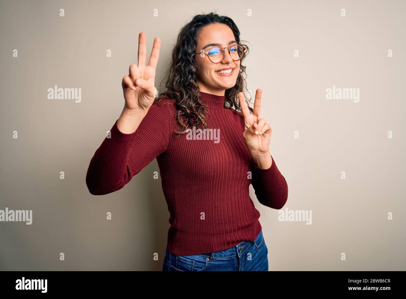 Beautiful woman with curly hair wearing casual sweater and glasses over ...