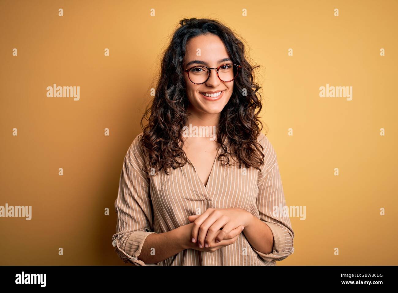 Beautiful woman with curly hair wearing striped shirt and glasses over ...