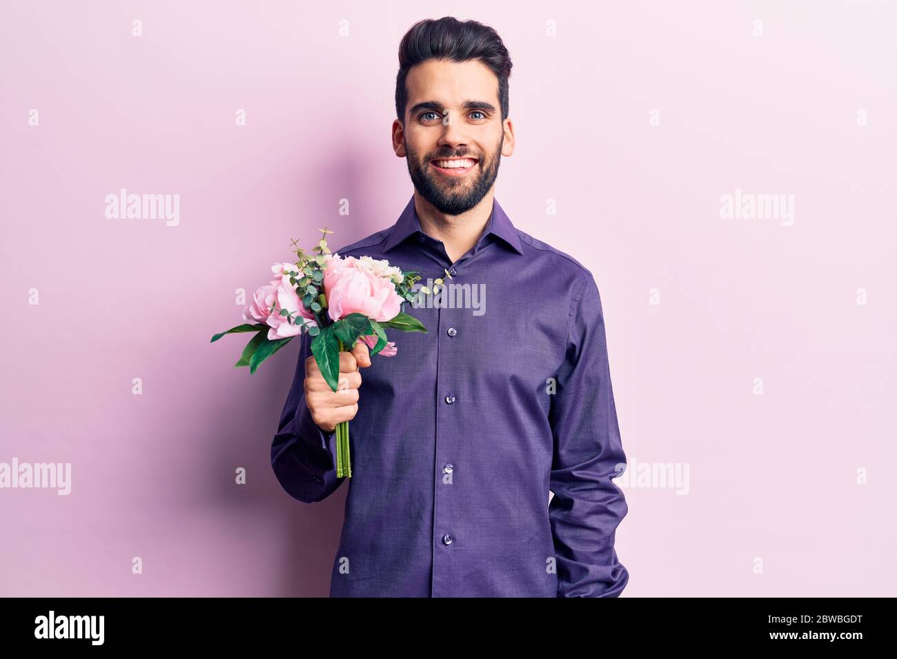 Young handsome man with beard holding bouquet of flowers looking ...