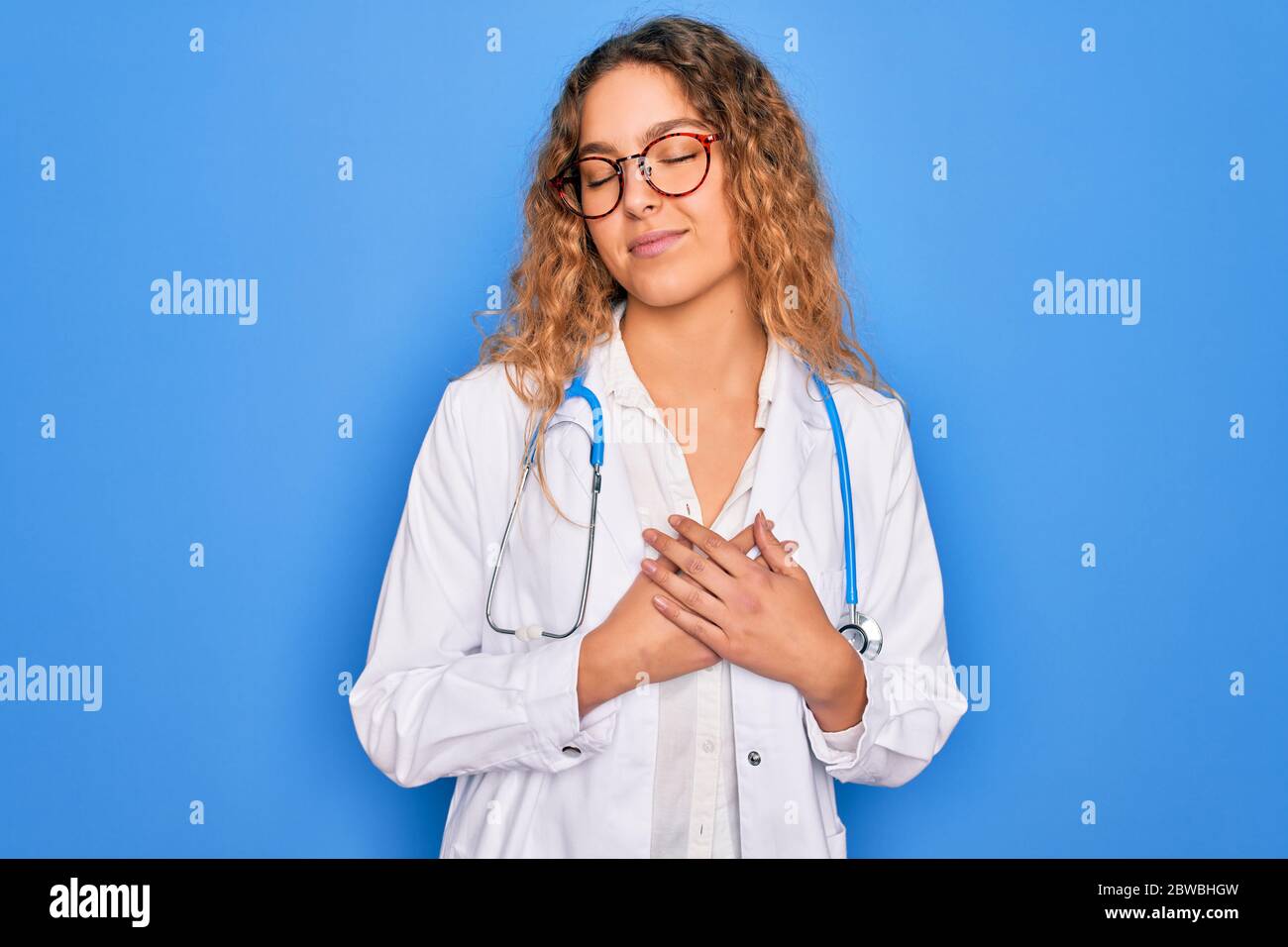 Young beautiful blonde doctor woman with blue eyes wearing coat and ...