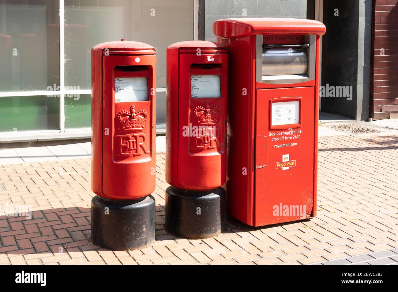 Royal Mail ER (Elizabeth Regina) freestanding pillar box post boxes and a franked mail and parcel business post box on London Road, Basingstoke, UK Stock Photo