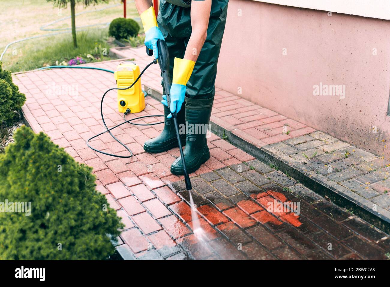 Man cleaning red, conrete pavement block using high pressure water