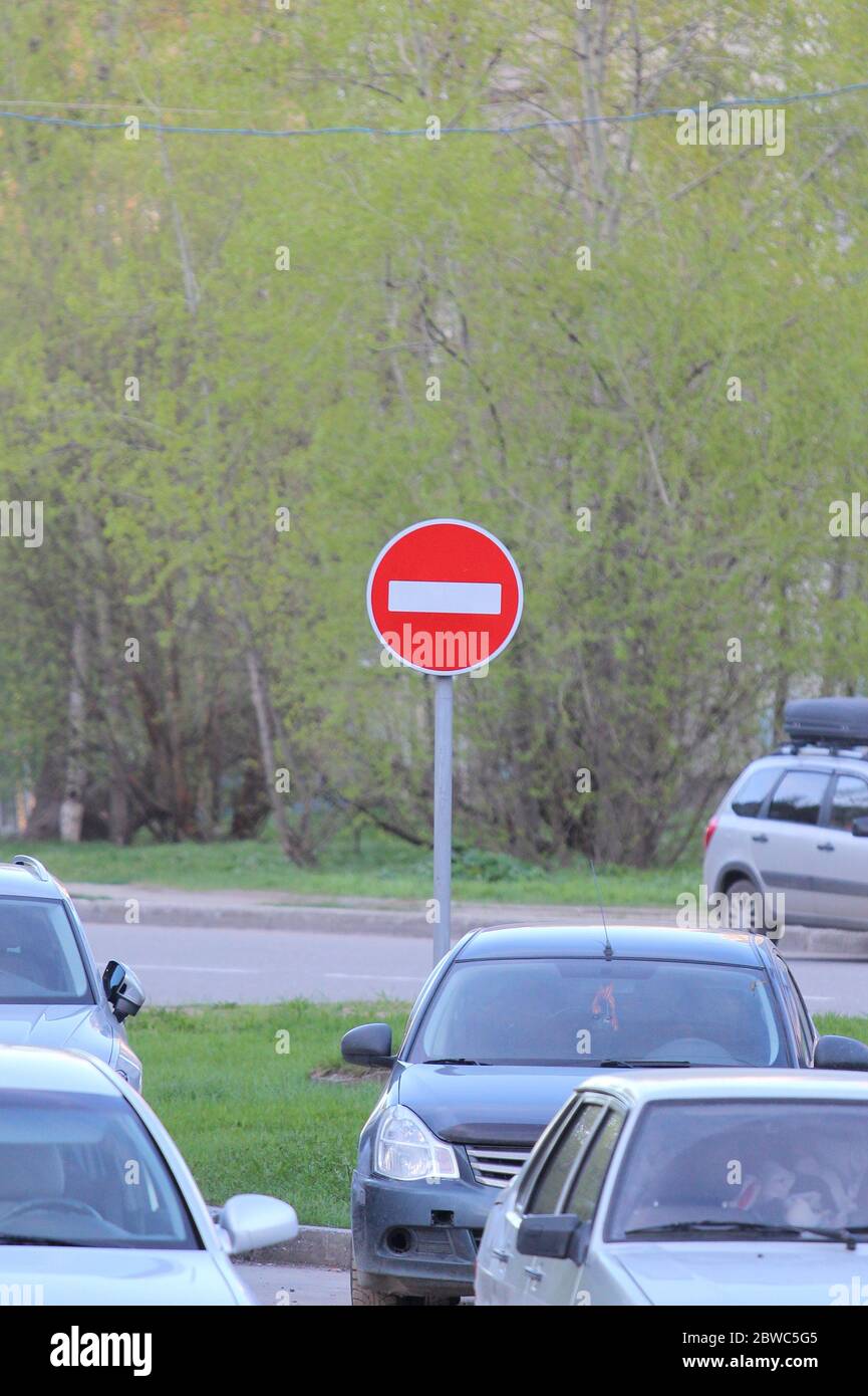 Red round road sign with white stripe prohibiting movement on a city street with cars. Do not enter. concept of prohibition, dead end, hopelessness and stop. Stock Photo