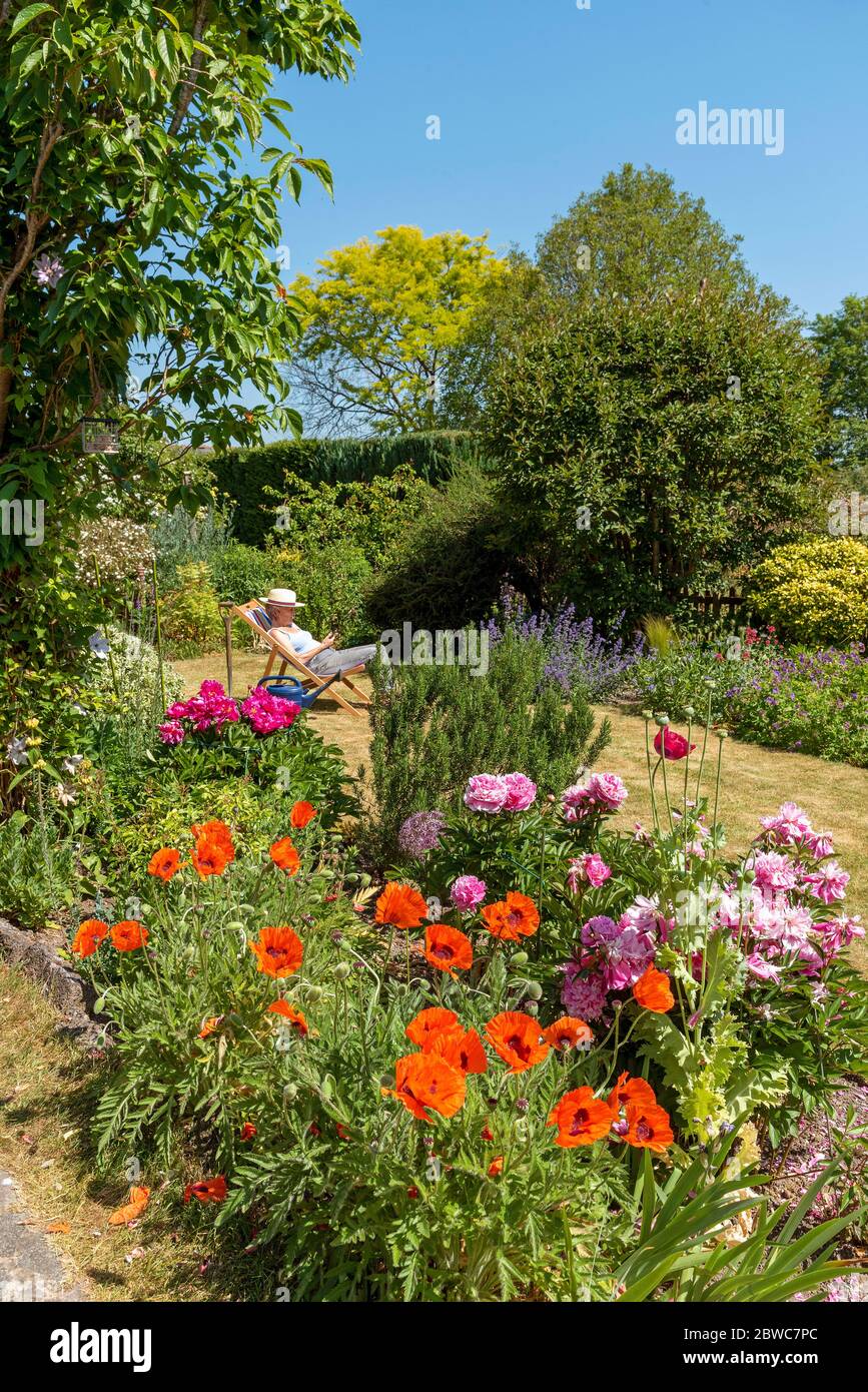 North Hampshire, England, UK. May 2020. An attractive English country garden and a woman in a deckchair. Hampshire, England UK. Stock Photo