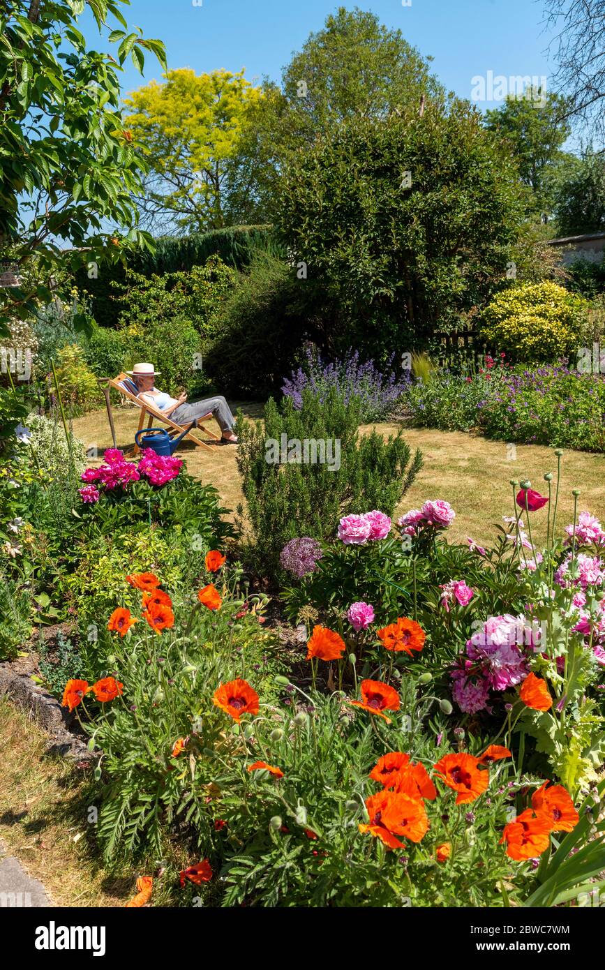 North Hampshire, England, UK. May 2020. An attractive English country garden and a woman in a deckchair. Hampshire, England UK. Stock Photo