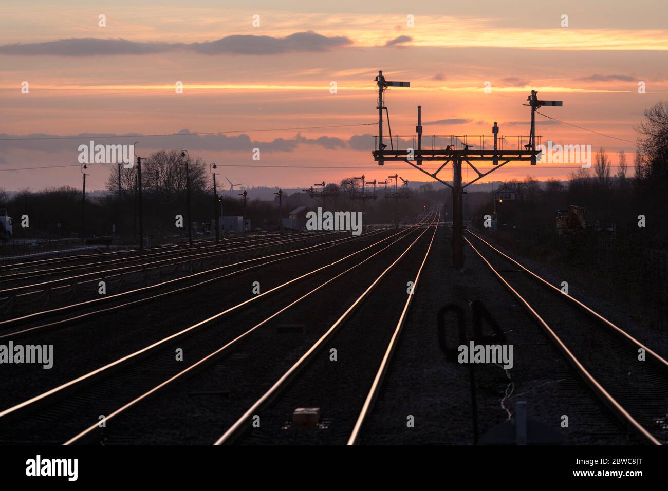 The large semaphore bracket signals at Barnetby, Lincs, making a silhouette with the rails glinting  in the sunset Stock Photo