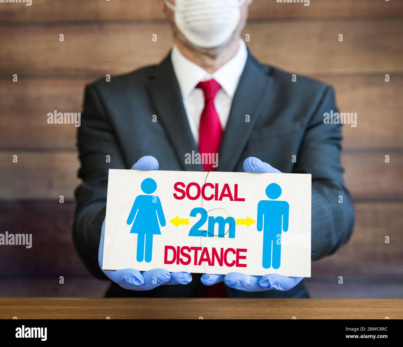 A doctor, businessman or employer wearing full ppe including face mask and blue surgical gloves with a sign ordering people to stay 2 metres away Stock Photo