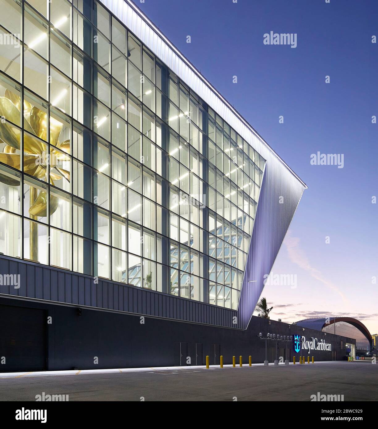 Exterior facade, lit up at sunset with view of sculptural propellor artwork inside. Royal Caribbean Miami Cruise Terminal, Miami, United States. Archi Stock Photo