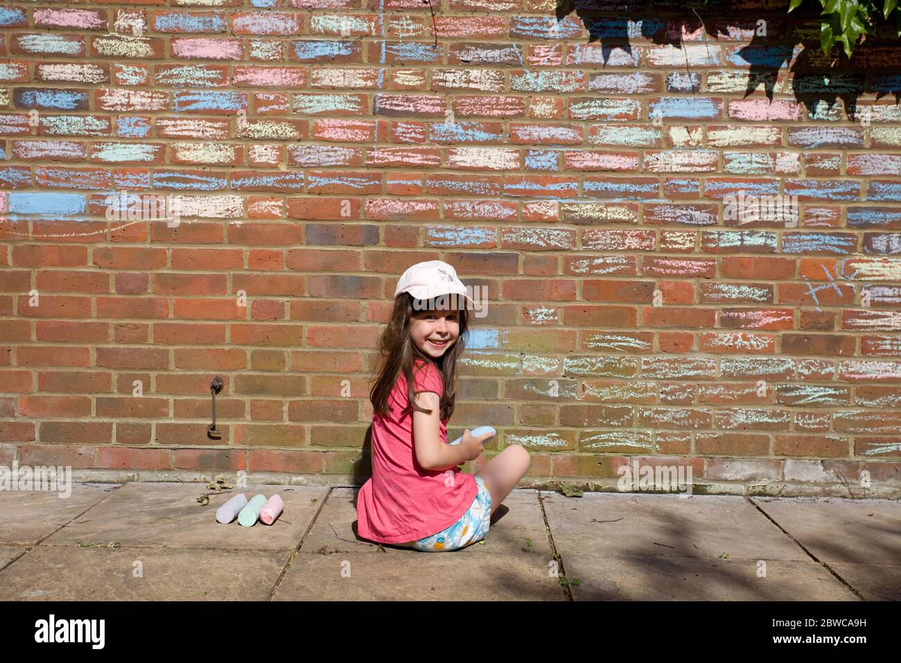 Young happy girl colouring in house bricks with chalk pastels, Uk Stock Photo