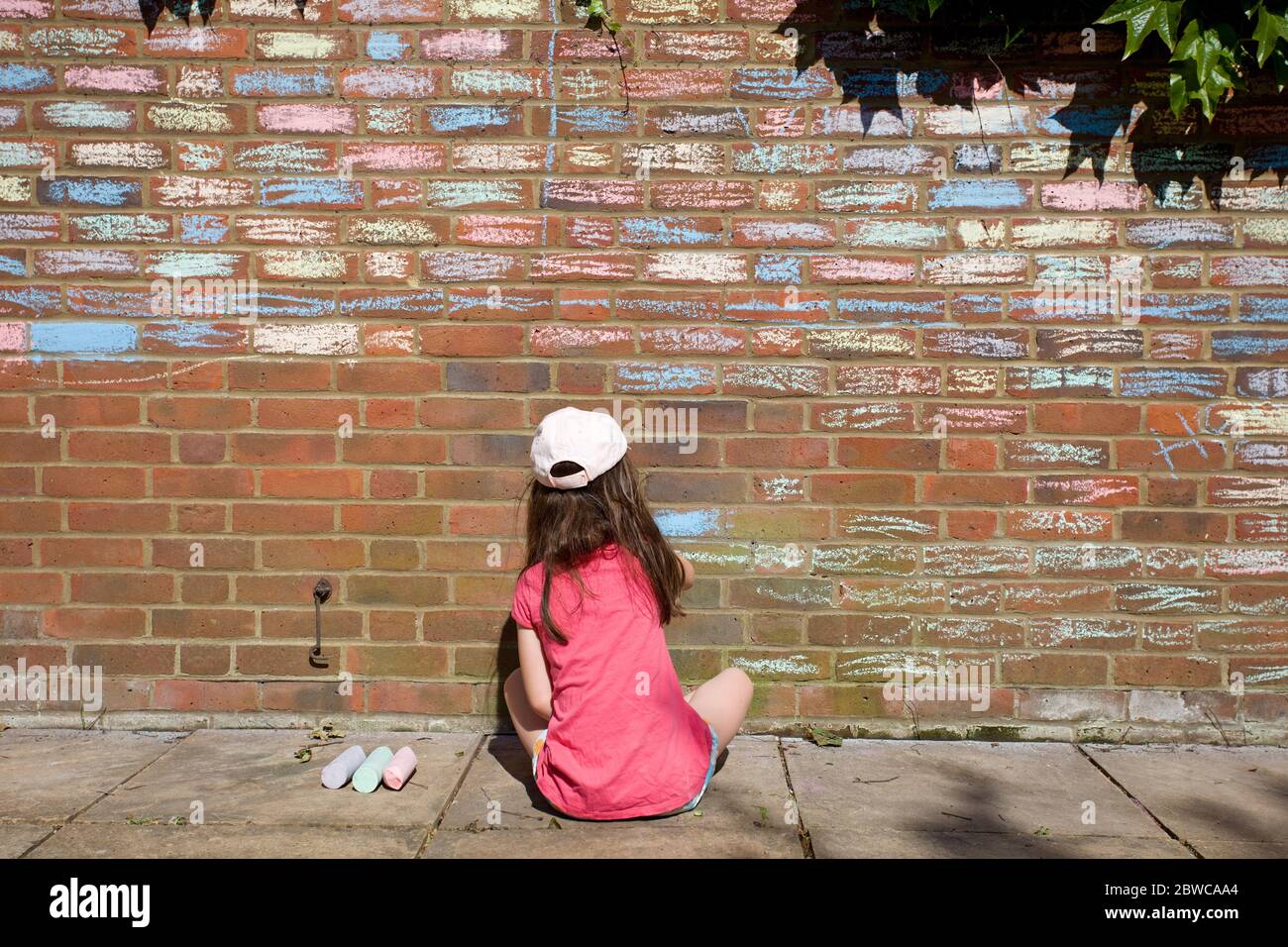 Young girl sat on floor applying chalk pastels to house bricks, England Stock Photo