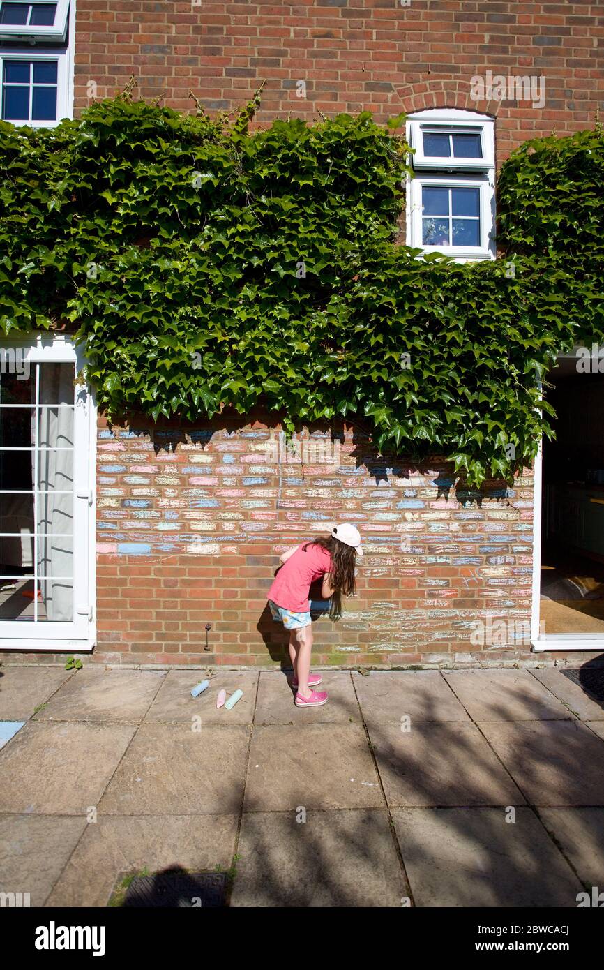 Young girl colouring in house bricks with chalk pastels, Uk Stock Photo