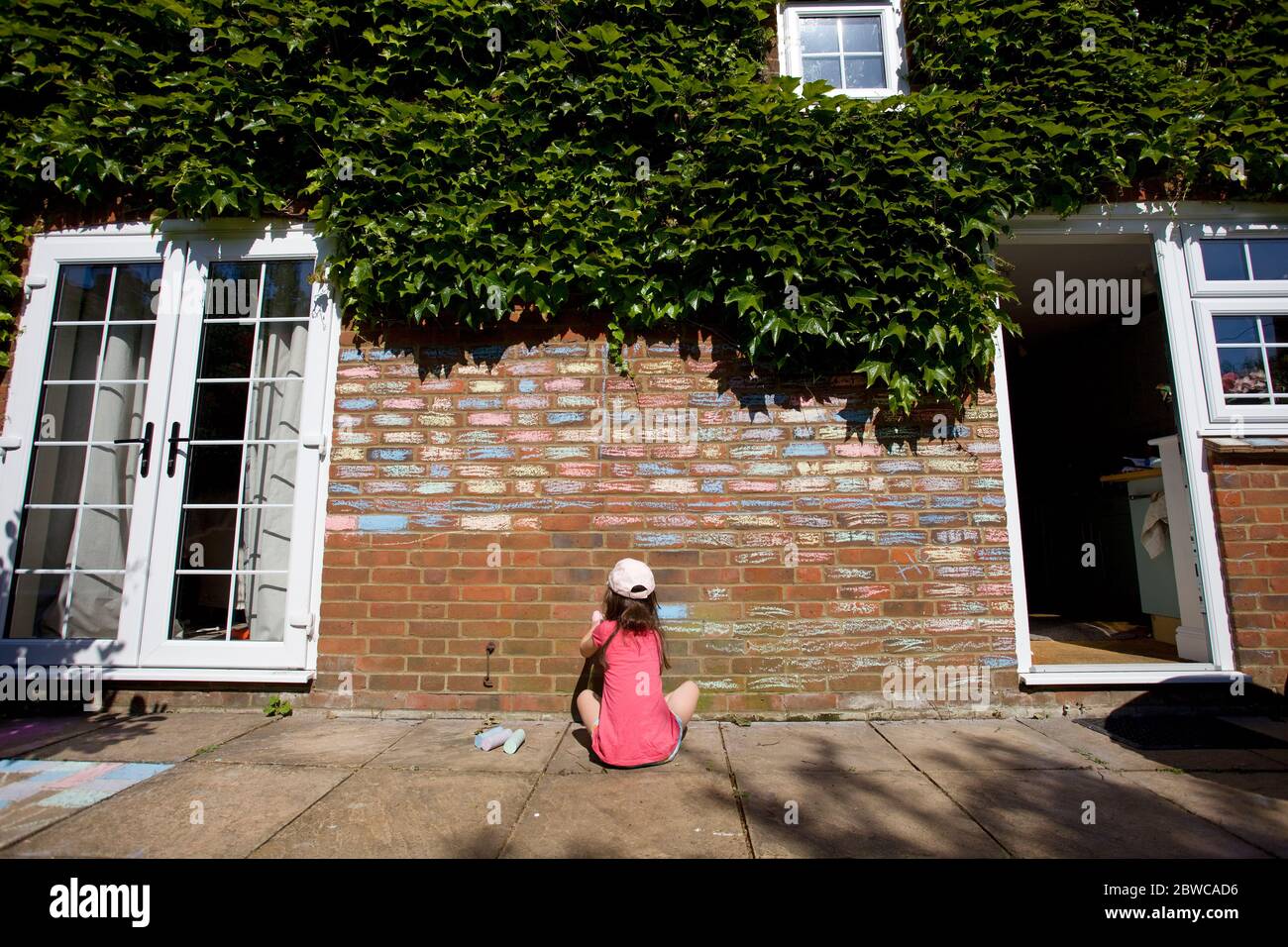 Young girl sat on floor colouring in house bricks with chalk pastels, England Stock Photo