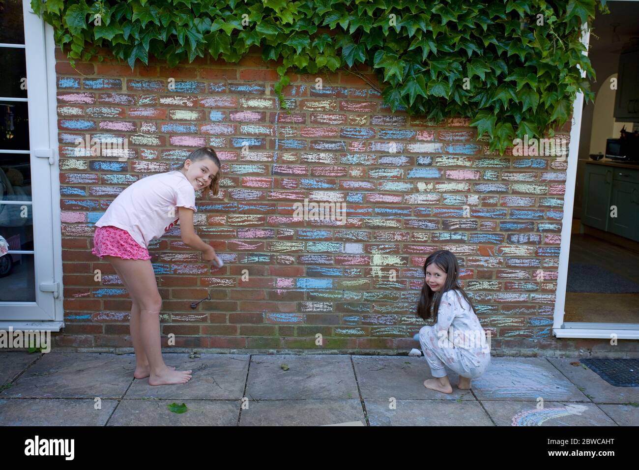 Young girls colouring in house bricks with chalk pastels, Uk Stock Photo