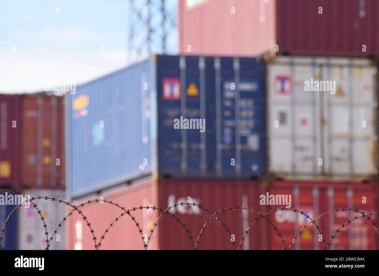 Freight shipping containers stacked up behind barbed wire at a busy European sea port Stock Photo