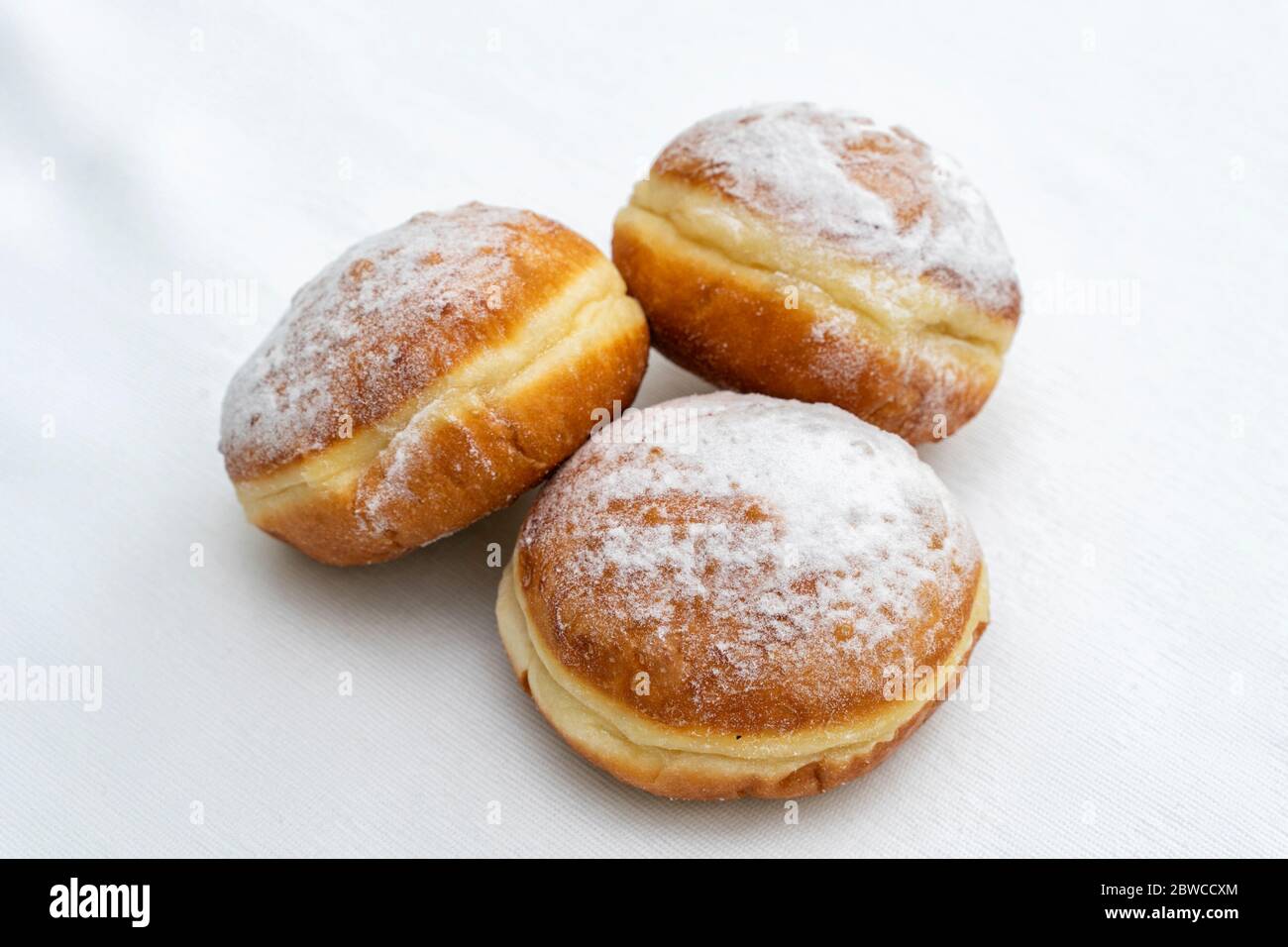 three donuts sprinkled with icing sugar on a light surface Stock Photo