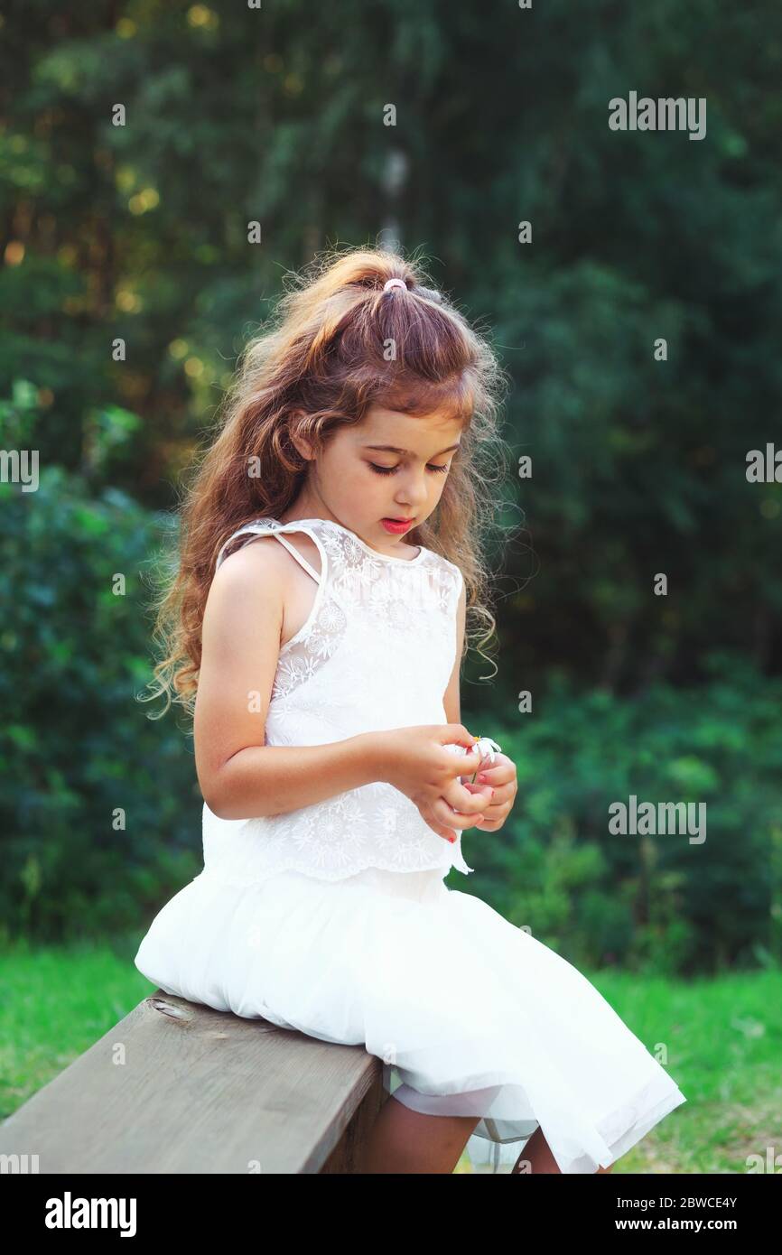 Beautiful little girl  playing with flowers in spring park. Happy cute child having fun outdoors at sunset. Stock Photo