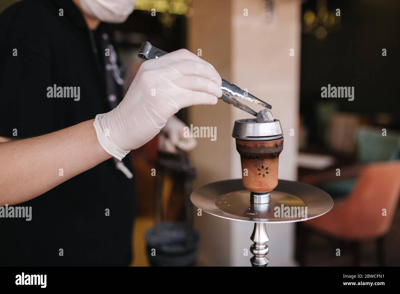 Close up of hookahman tup coal in hookah. Man in glowes use tweezers
