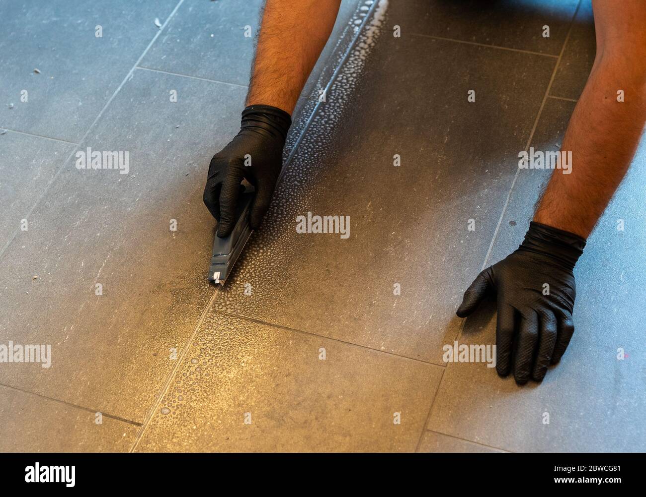 A professional cleaner cleaning grout with a brush blade and foamy soap ...