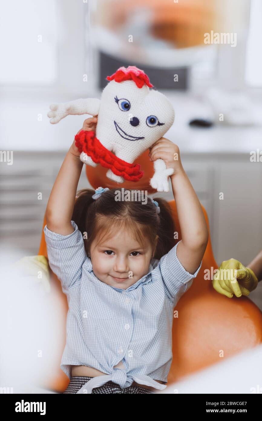 Cute little girl playing with knitted tooth toy while sitting on chair