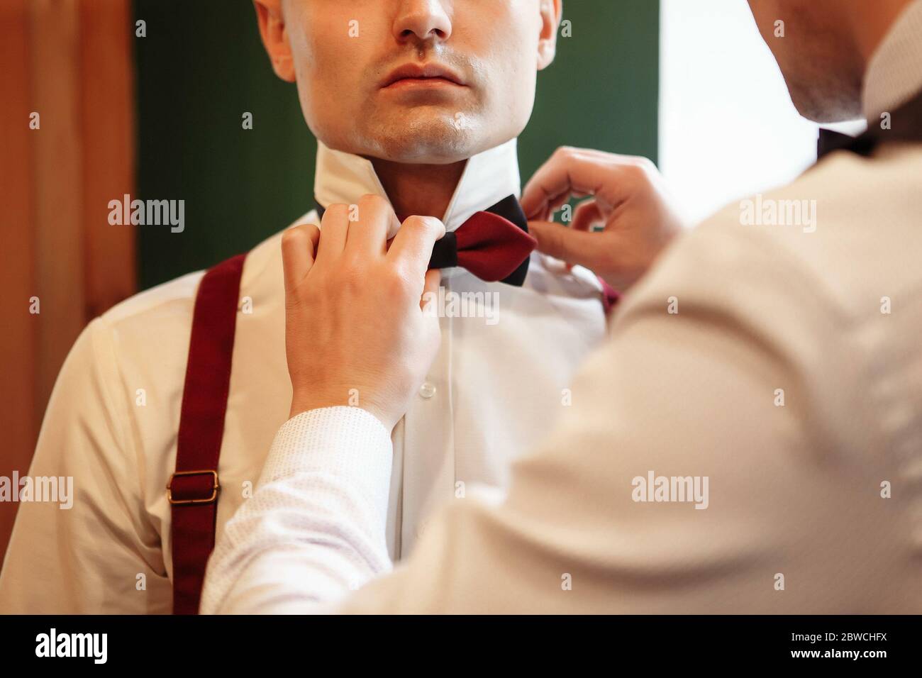 The groom in a black suit corrects a butterfly. Close-up of hands and neck. Wedding dresses Stock Photo