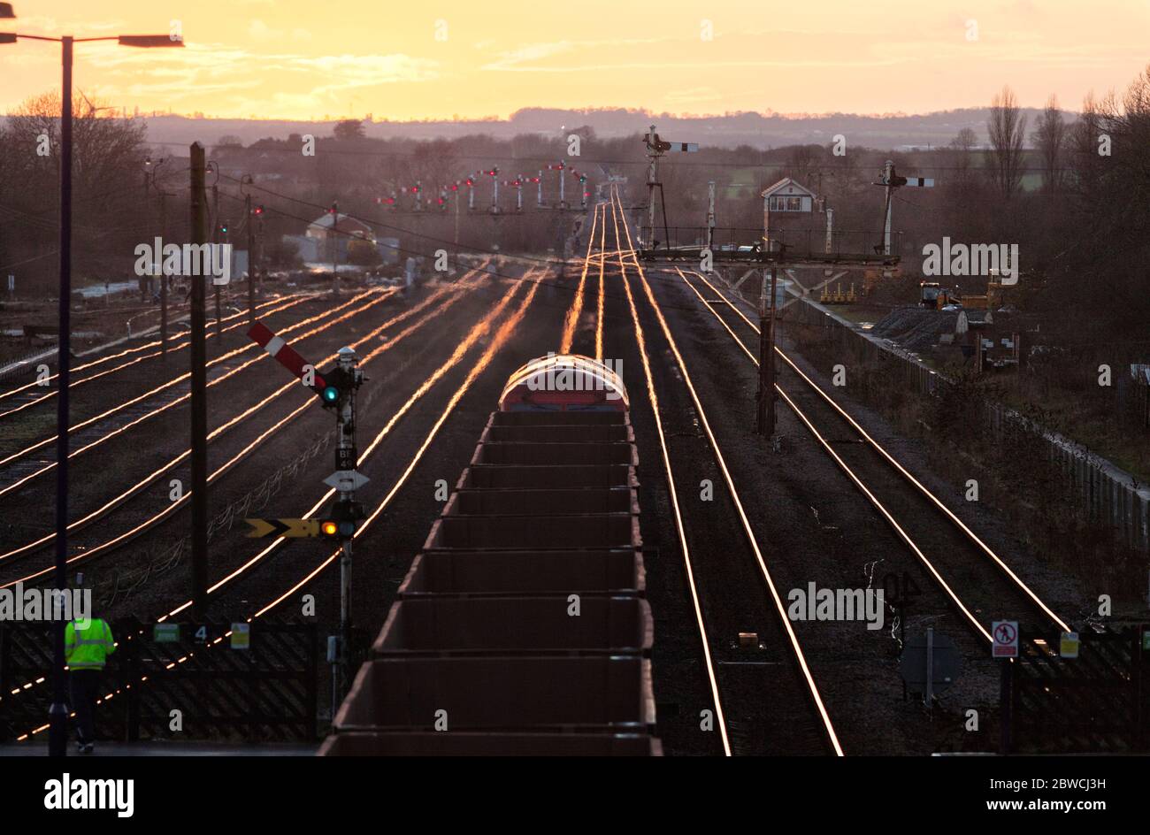 Freight train carrying Iron Ore passing The mechanical semaphore signals at Barnetby with the setting sun glinting off the rails Stock Photo