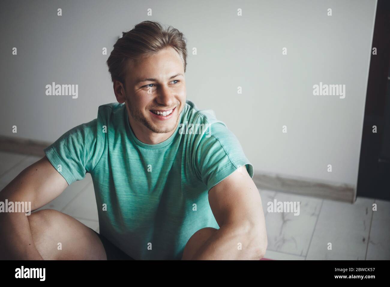 Blonde caucasian man wearing sportswear is smiling while resting after doing home gym exercises Stock Photo