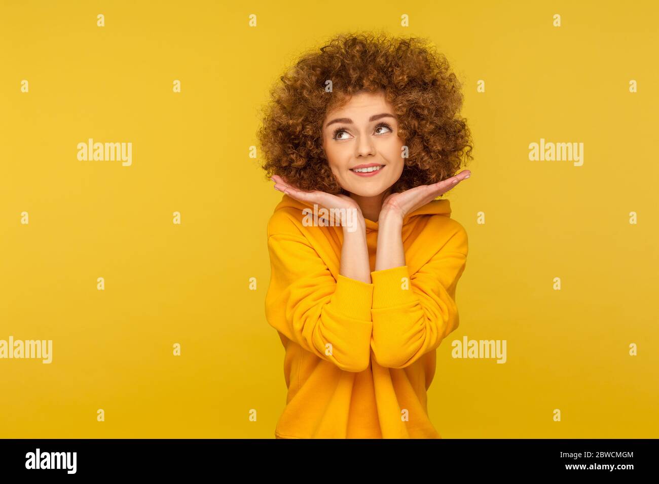 Portrait of lovely playful curly-haired young woman in urban style hoodie showing her clean fresh face with makeup, beauty and skin care concept. indo Stock Photo