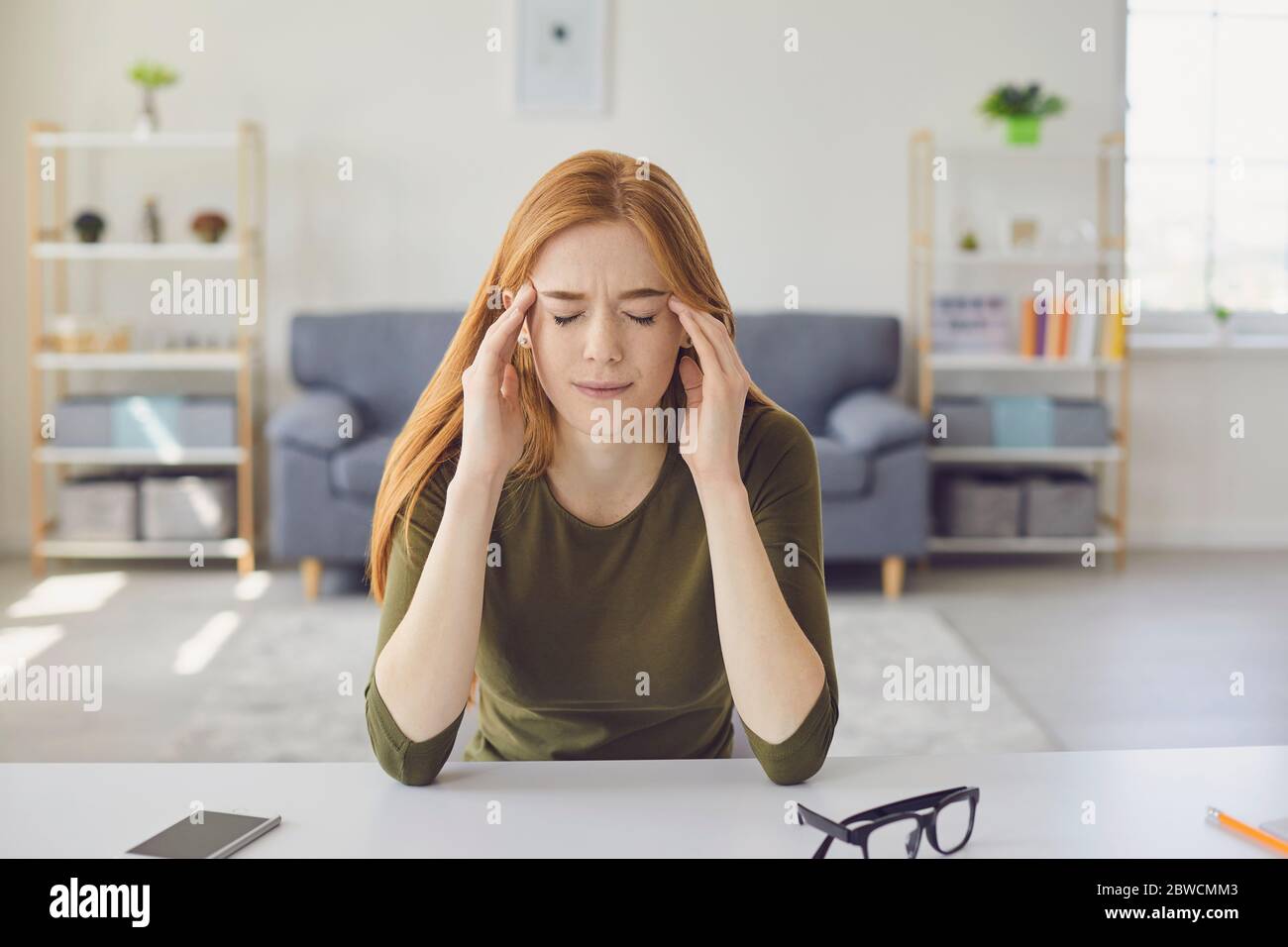 Beautiful girl feeling unwell, calling her doctor online from home. Young woman on video chat with health care provider.Headache. Stock Photo