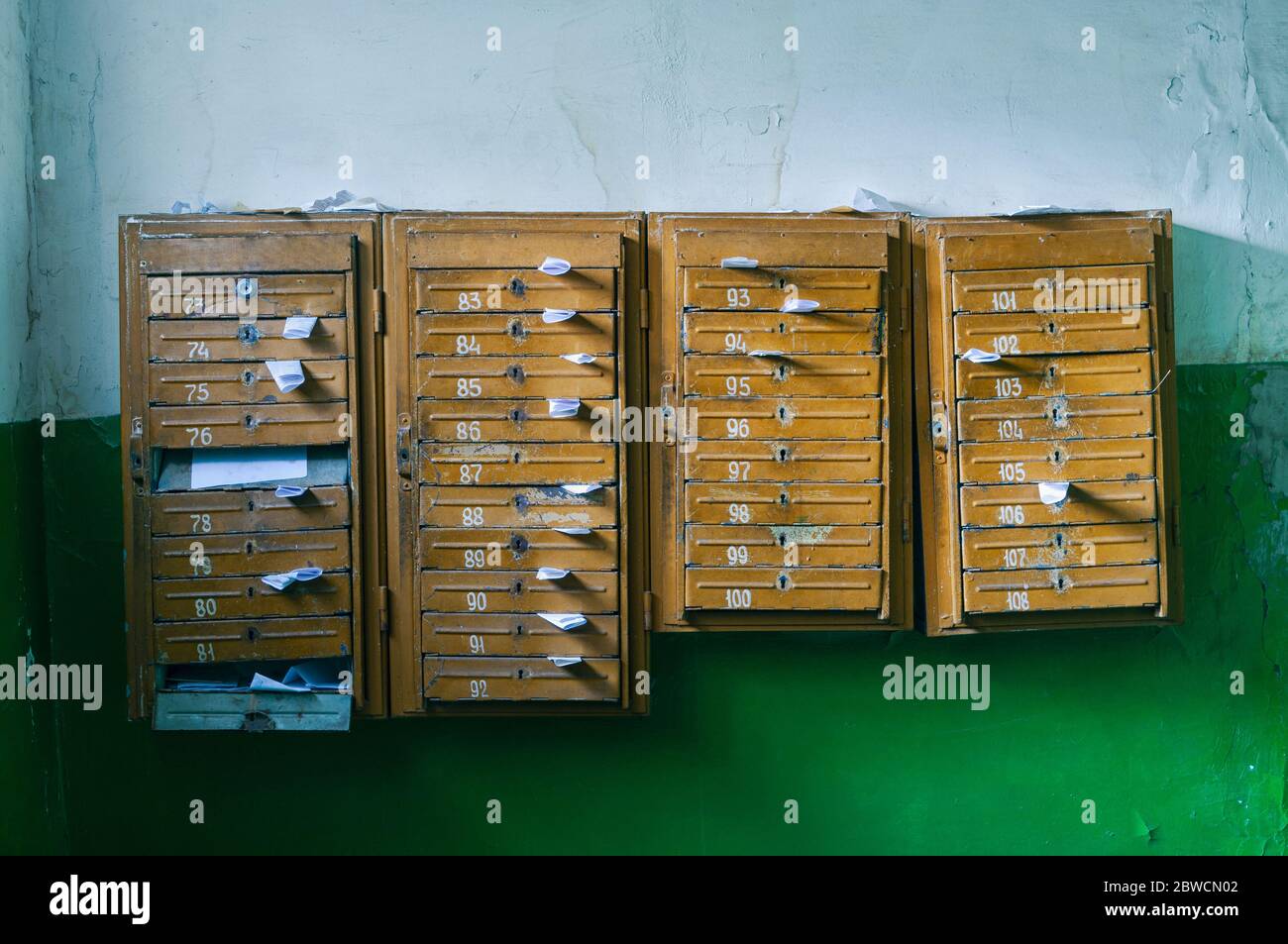 Old mailboxes in the entrance hall of a residential house filled with white paper flyers. Mass mailing concept. Stock Photo