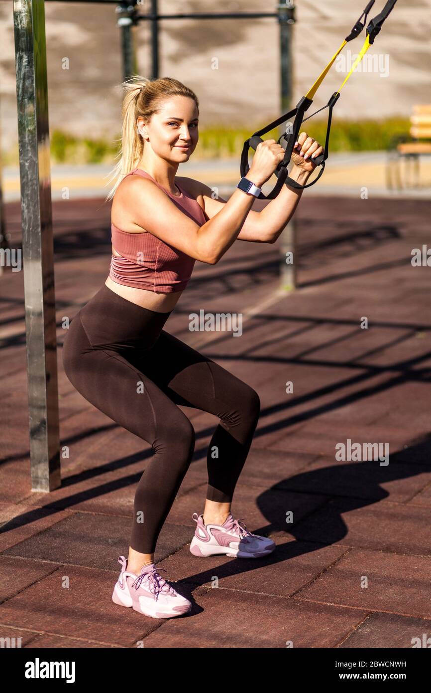 Strong athletic girl training outdoor doing squats with trx suspension straps and smiling to camera full body workouts for muscle build fat burning Stock Photo Alamy