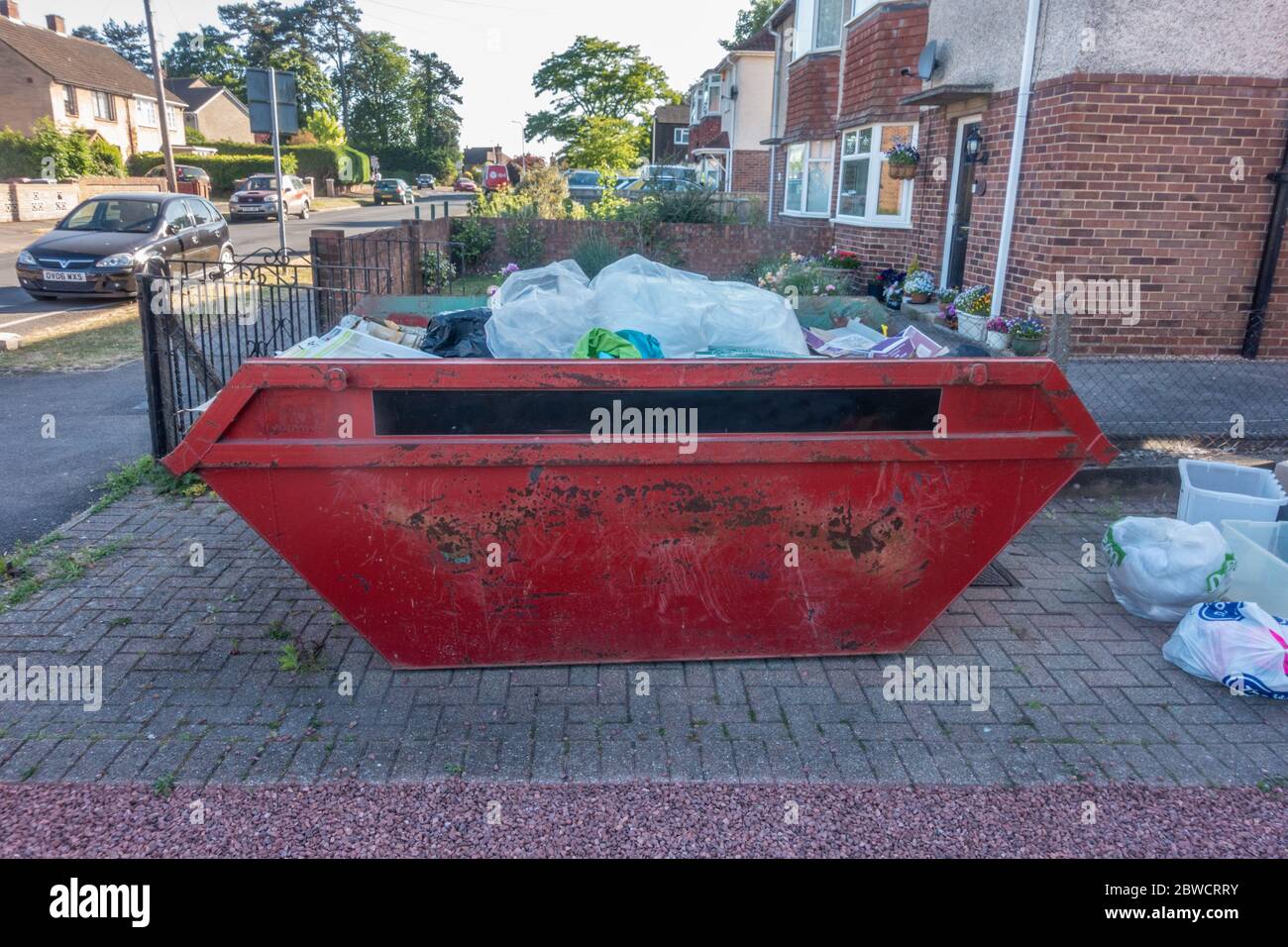 A skip on the driveway of a residential house full of rubbish as the home owner is having a clear out of hoarded rubbish. Stock Photo