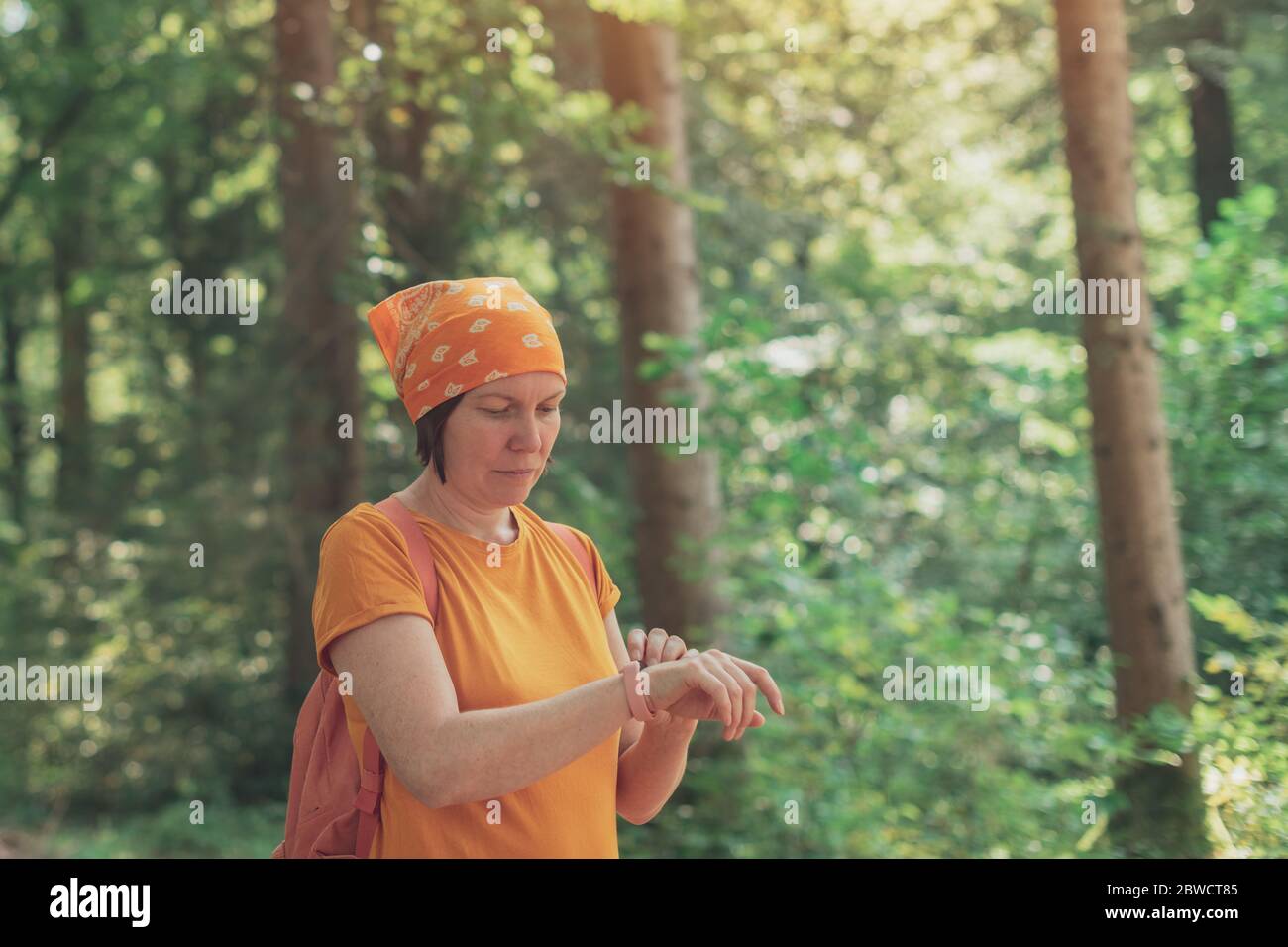 Woman hiker using smart fitness tracker wristband during trekking in nature. Female hiking in forest and checking on her modern gadget. Stock Photo